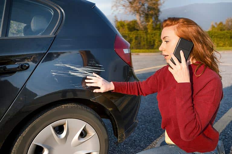 Motorista ao telefone percebendo arranhão no carro
